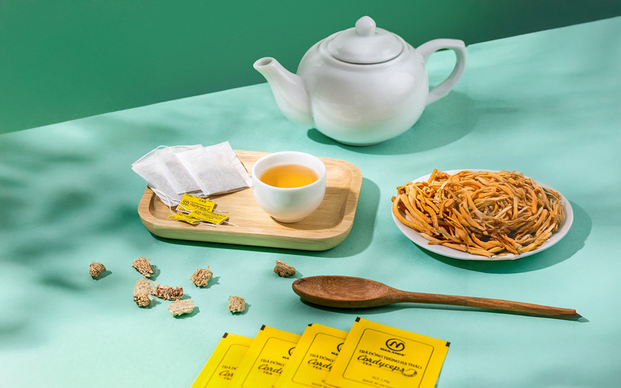 Các gói trà đông trùng hạ thảo túi lọc Mailands đang được đặt trên bàn kèm theo ấm pha trà, chén trà đông trùng hạ thảo.